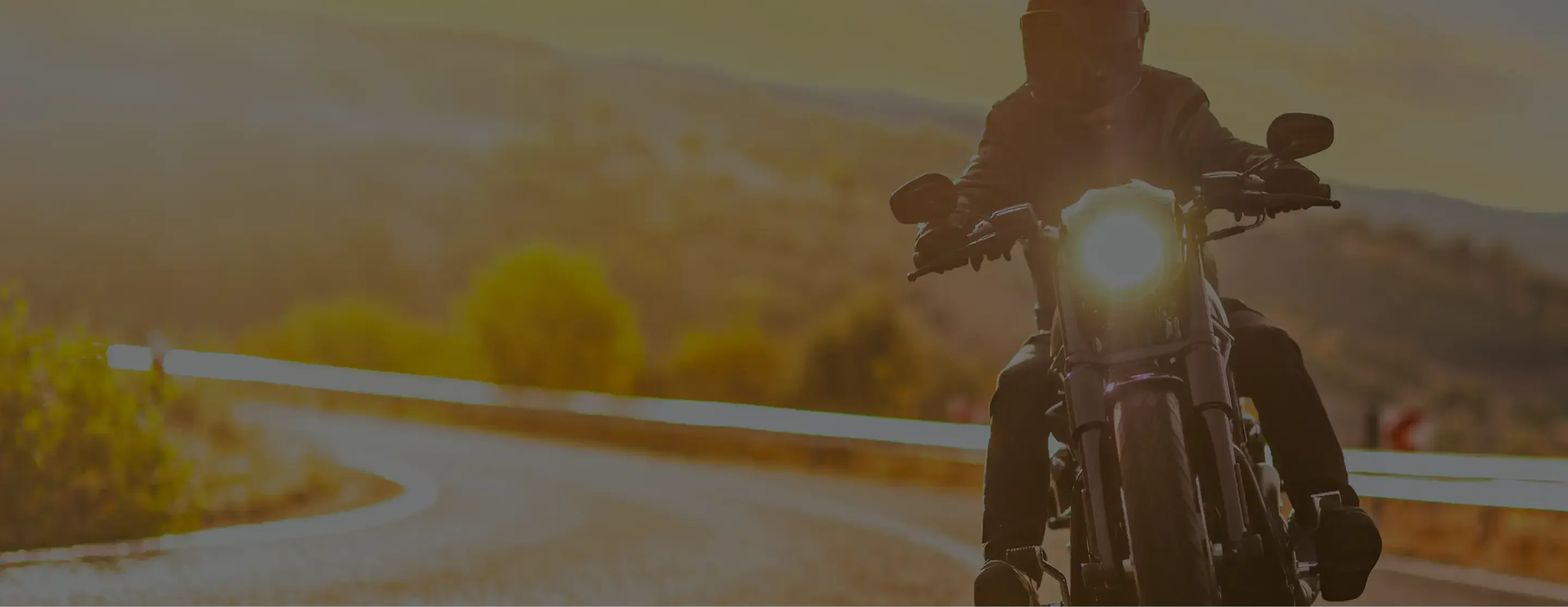 A motorcyclist rides a bike on a winding road at sunset, highlighting freedom and adventure in a scenic landscape.