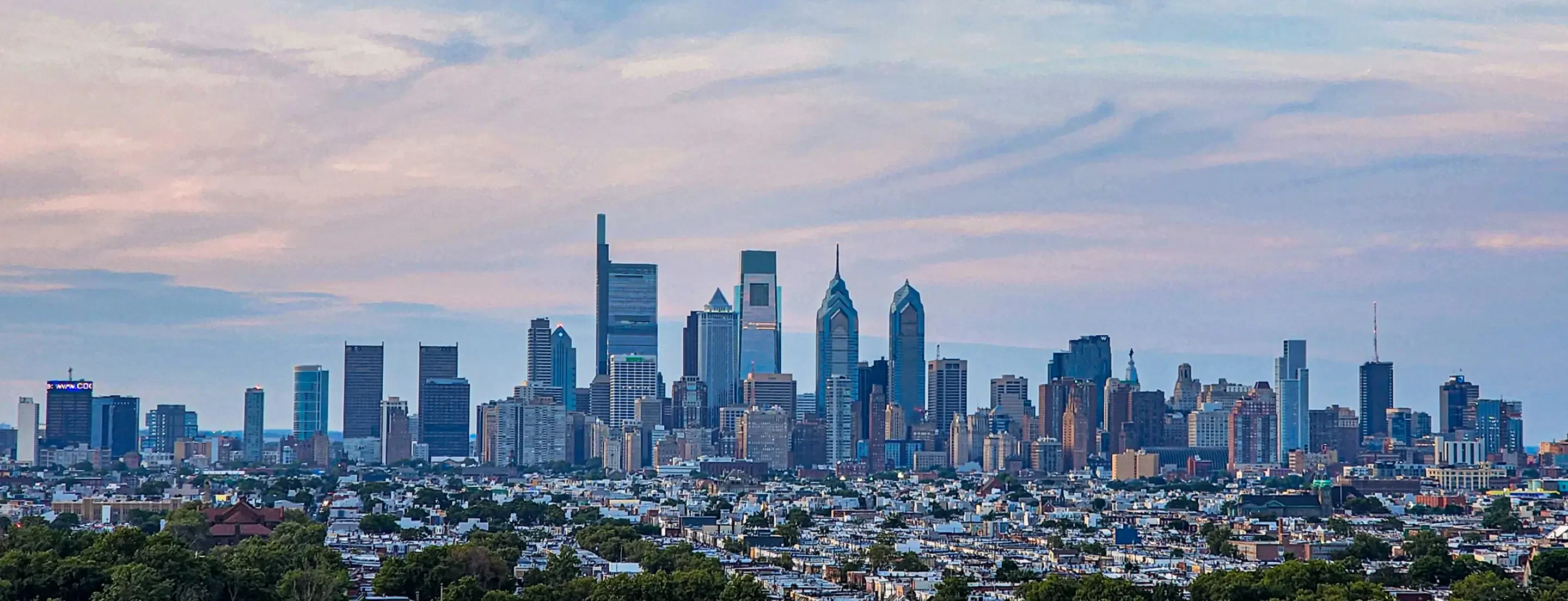 Panoramic view of Philadelphia's skyline under a pastel sky, showcasing a mix of modern skyscrapers and historic buildings.